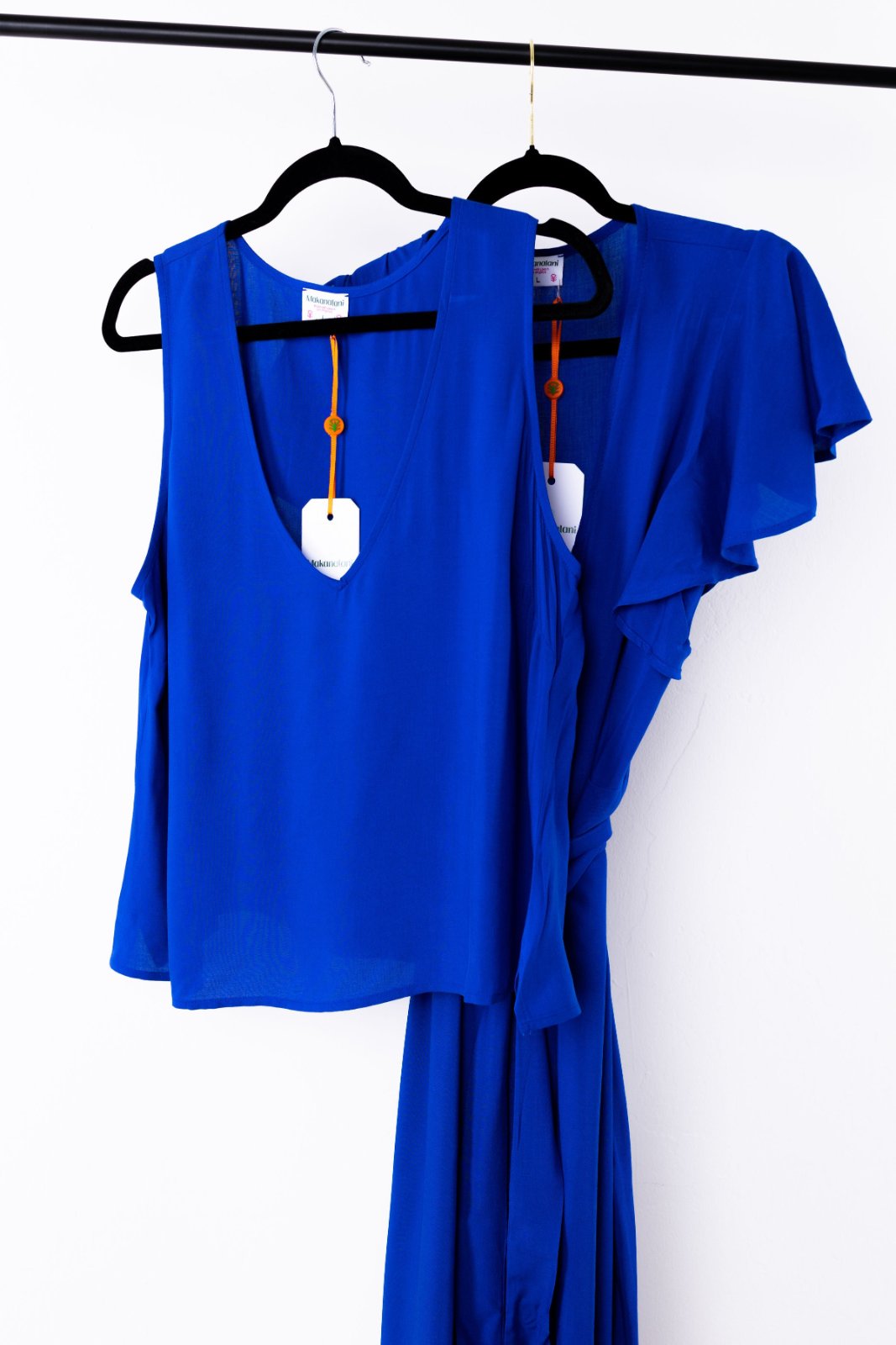 Blue dress with ruffled sleeves next to a blue tank top on hangers against a white background