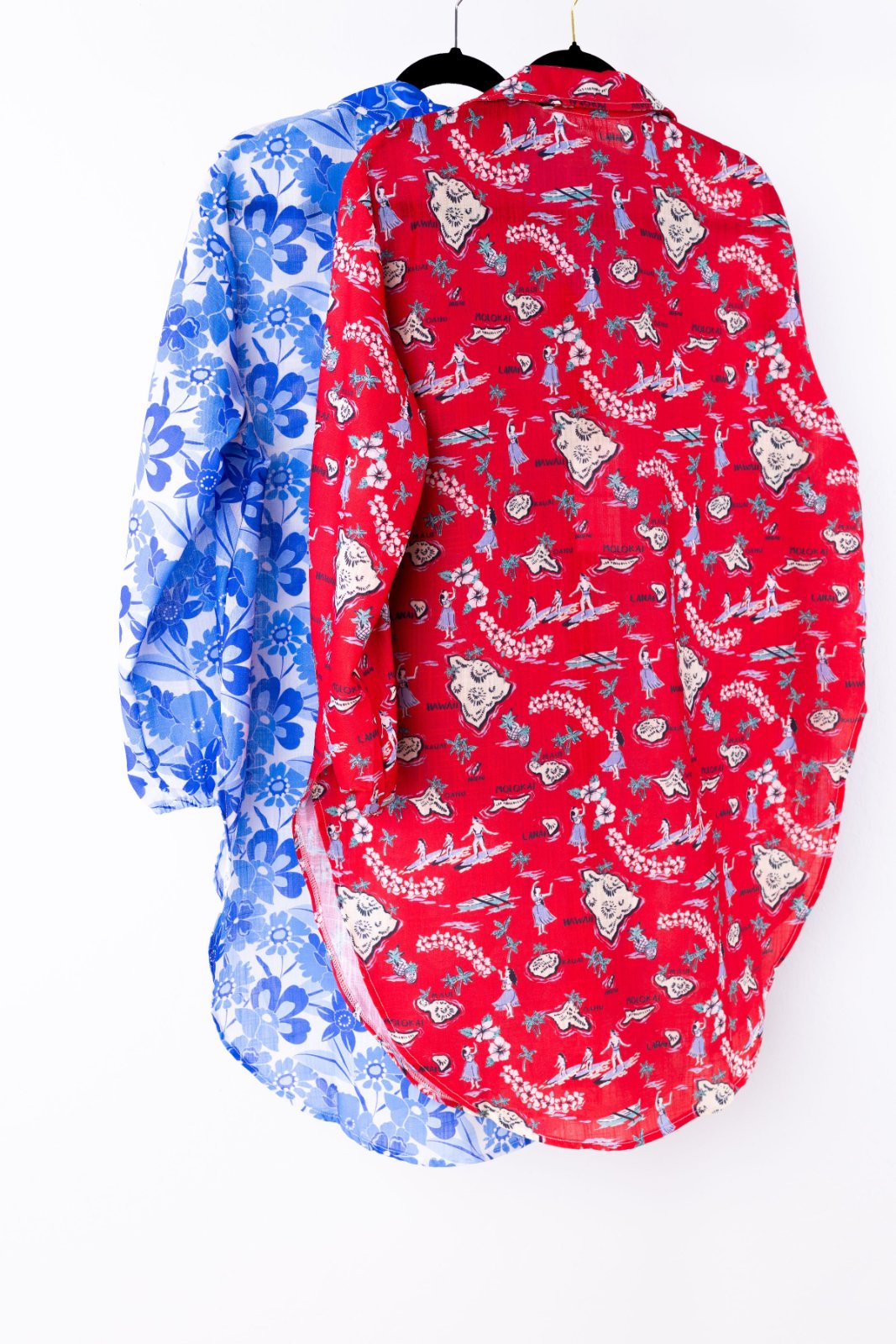 Two swim cover-ups, one red with patterns and one blue with patterns, on hangers against a white background.