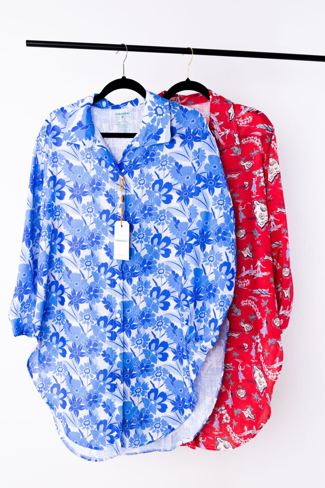 Two floral-patterned swim cover-ups, one blue and one red, hanging on a rack against a white background.