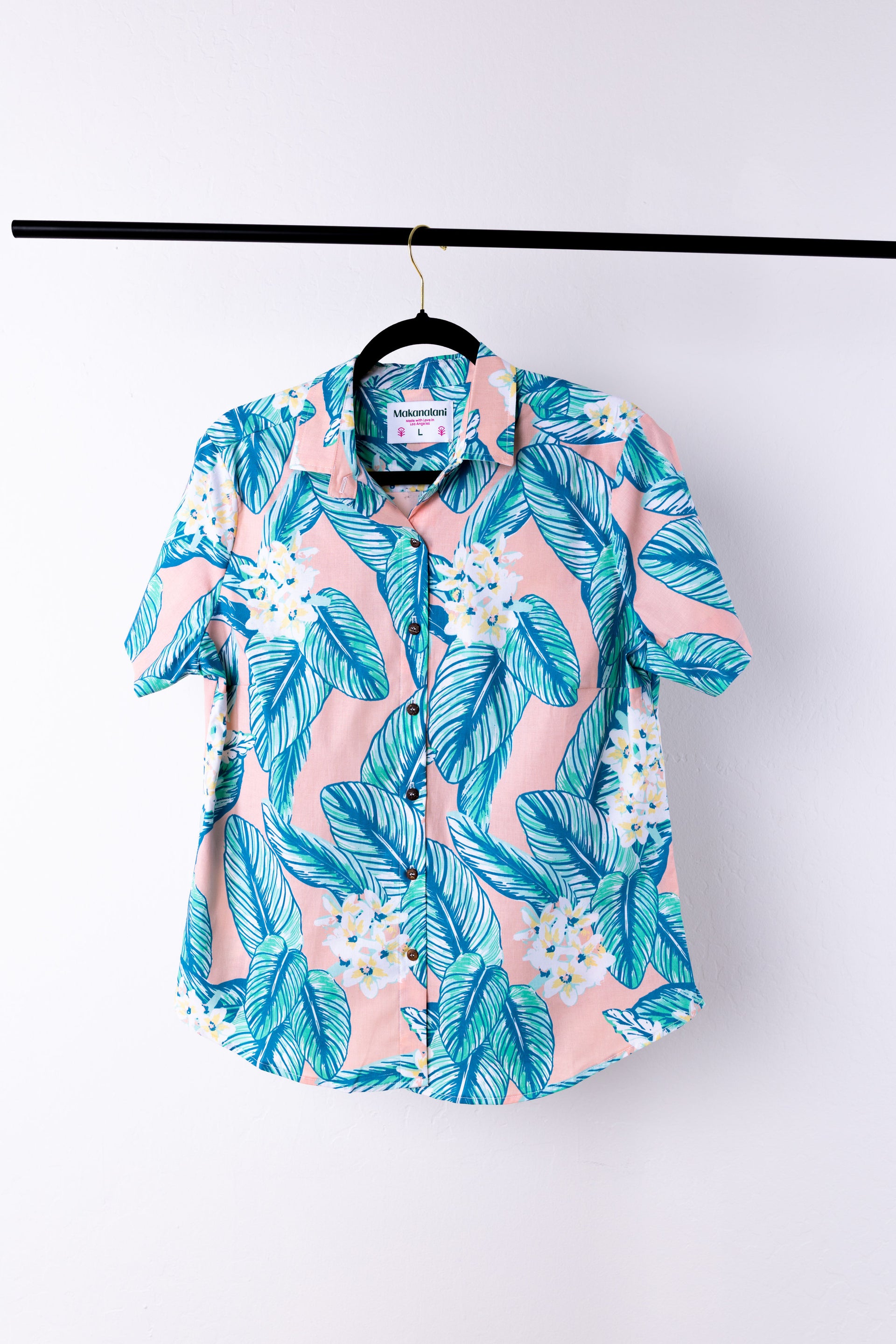 Hawaiian shirt with blue and pink leaf pattern on a hanger against a white background