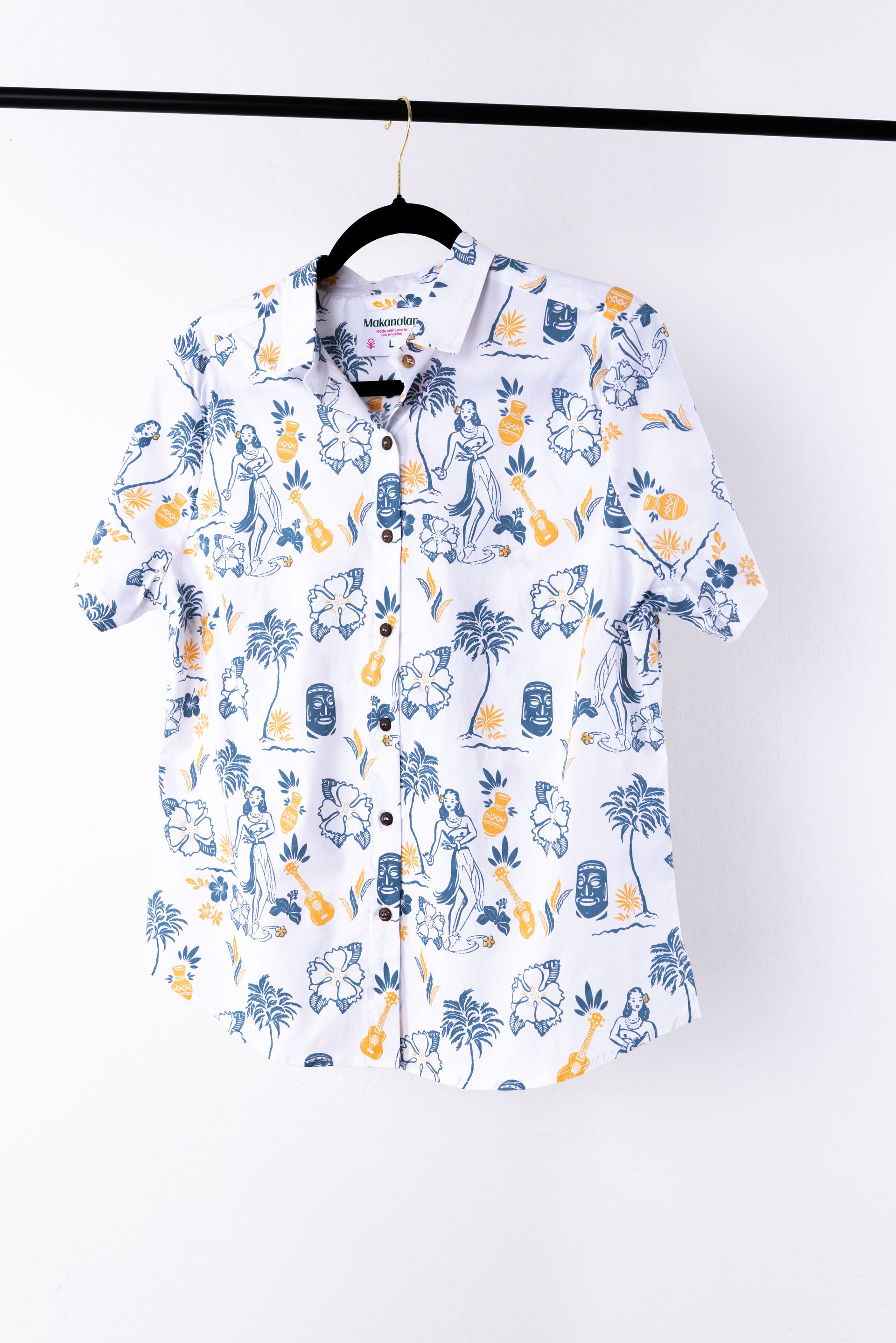 White shirt with colorful Hawaiian print hanging on a black hanger against a white background