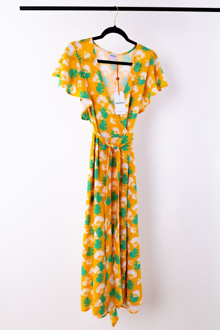 Yellow dress with green floral pattern on a hanger against a white background