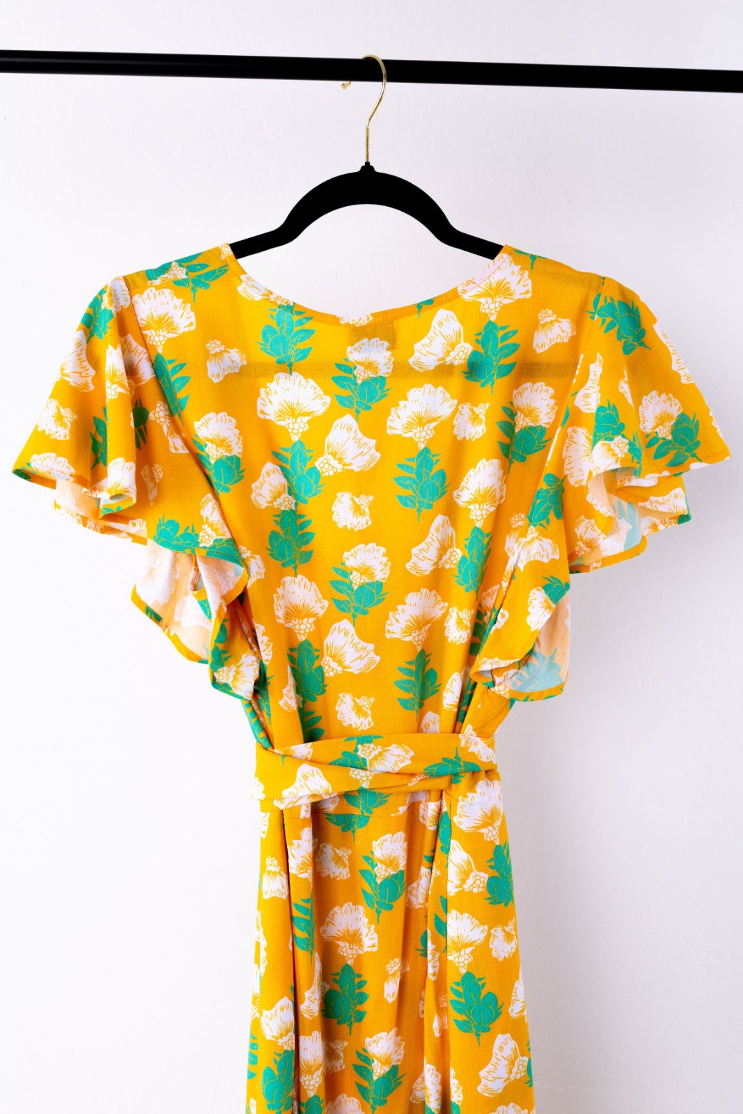 Yellow dress with floral pattern on a hanger against a white background
