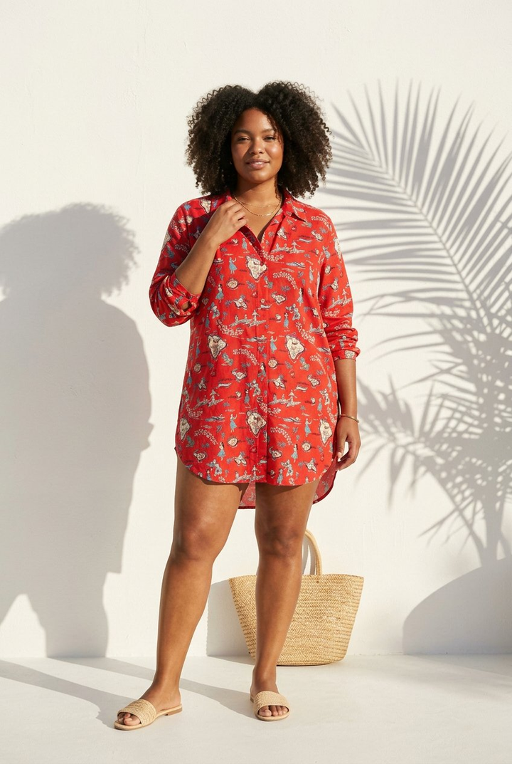 Woman wearing a red floral dress standing against a white background with palm leaves.