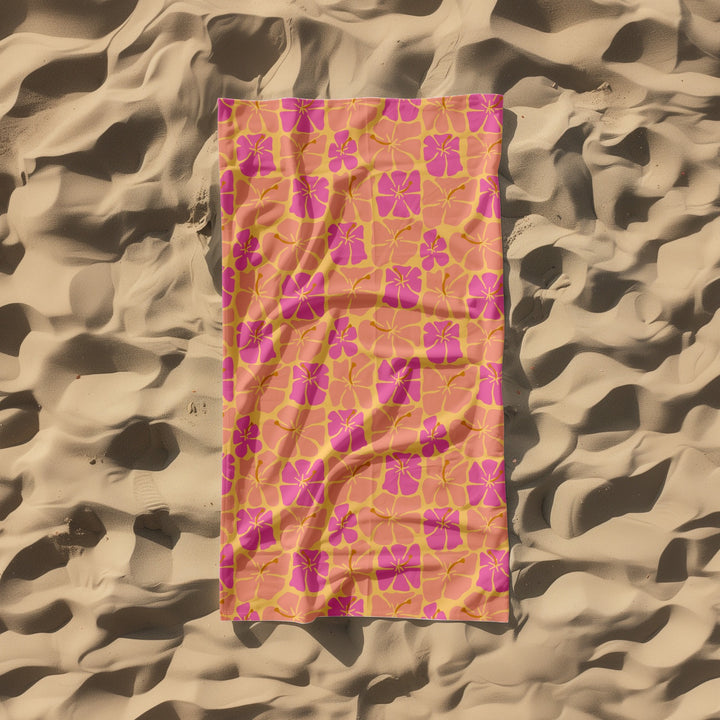 Pink and orange floral patterned towel on a sandy background
